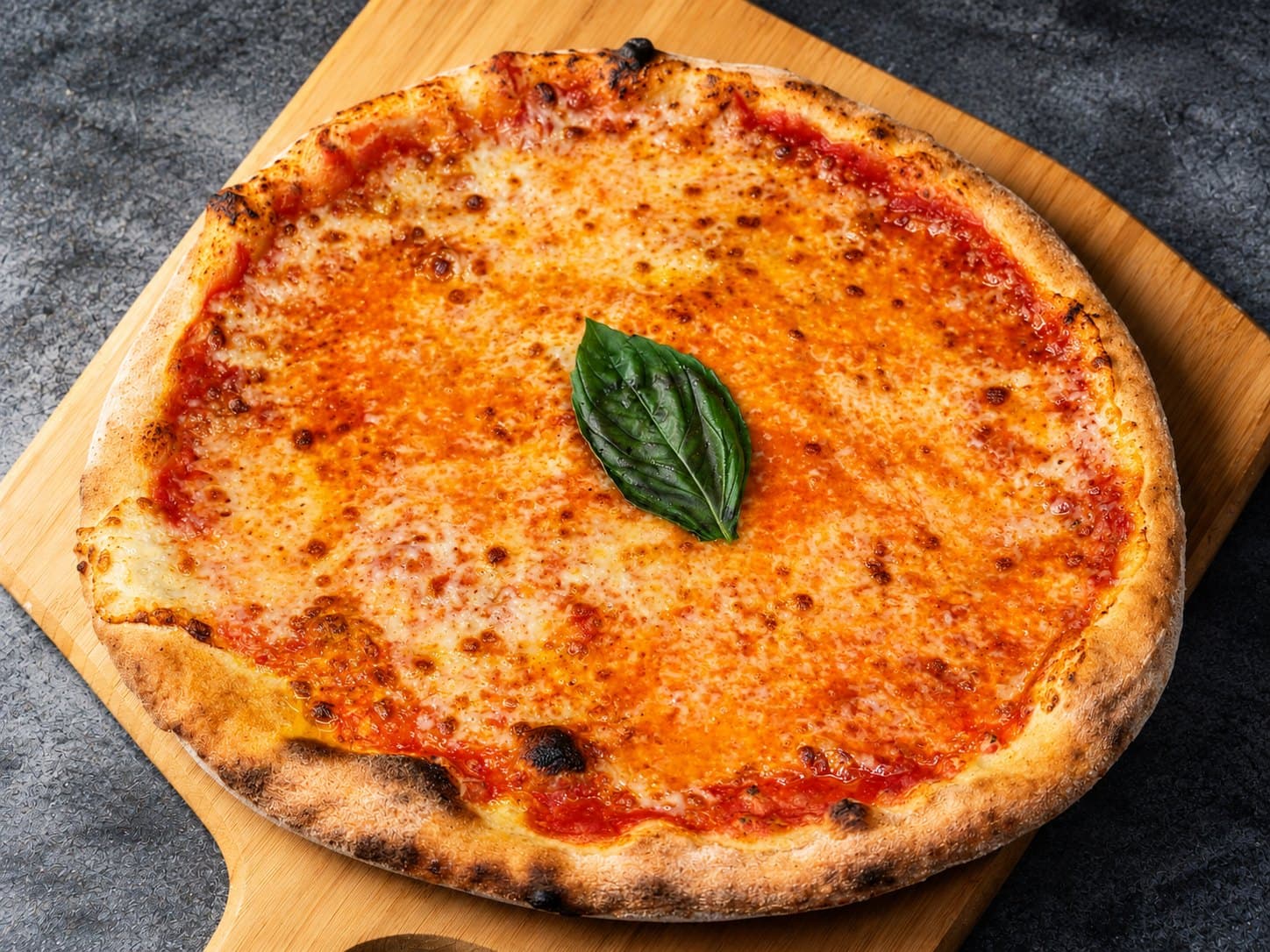 Pizza margherita appena sfornata su una pala di legno, con una foglia di basilico fresco